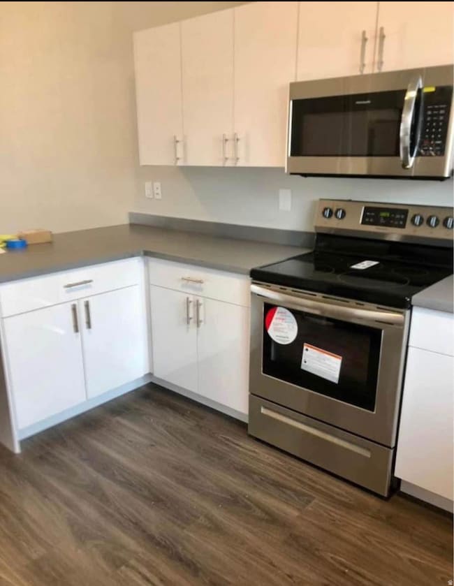 Kitchen featuring stainless steel appliances, white cabinets, dark wood finished floors, dark countertops, and a peninsula