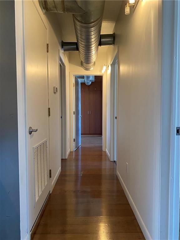 Hallway with dark wood-type flooring and baseboar