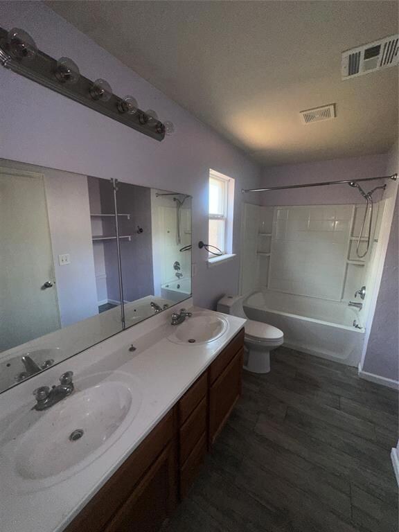 Bathroom featuring shower / bathtub combination, double vanity, toilet, wood finished floors, and a textured ceiling