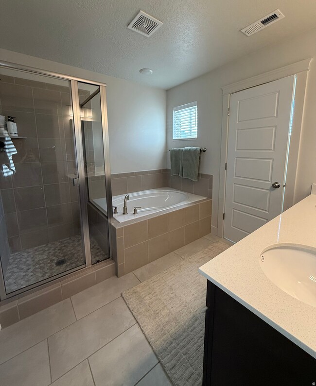 Full bathroom featuring double vanity, a stall shower, a bath, light tile patterned flooring, and a textured ceiling