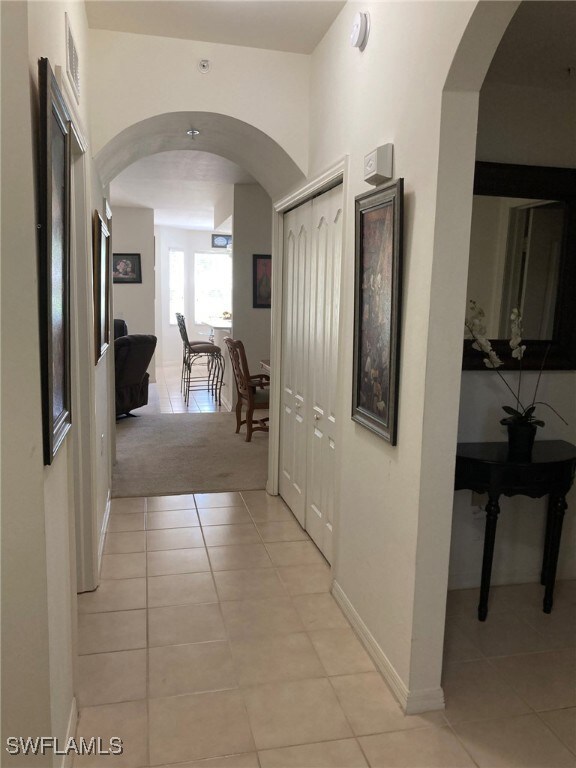 Hall featuring light tile patterned floors, arched walkways, and baseboards
