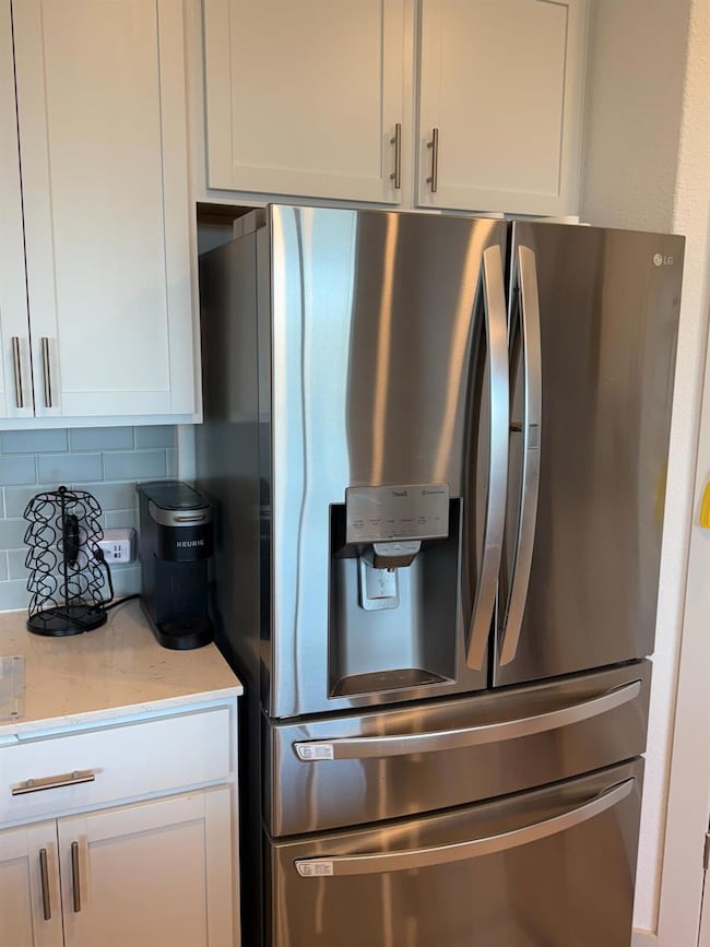 Kitchen view of stainless steel fridge with ice dispenser, white cabinetry, and light stone counters