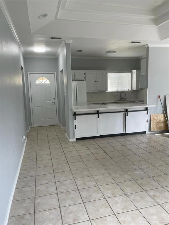 Kitchen featuring light tile patterned floors, light countertops, ornamental molding, white cabinets, and freestanding refrigerator