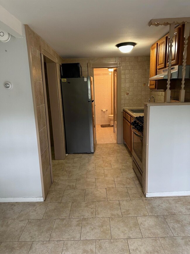 Kitchen featuring stainless steel appliances, brown cabinetry, light countertops, and under cabinet range hood