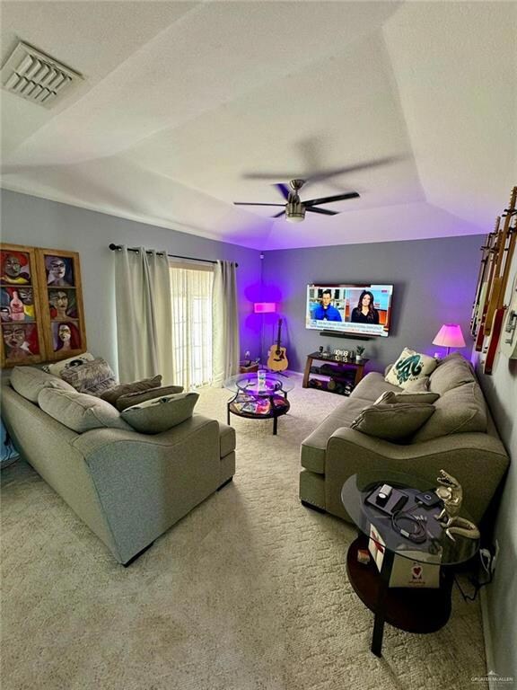 Living room featuring a textured ceiling, a raised ceiling, light colored carpet, and ceiling fan
