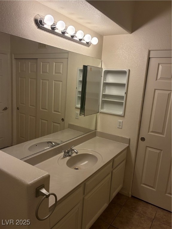 Bathroom featuring dark tile patterned flooring, vanity, a textured ceiling, and a textured wall
