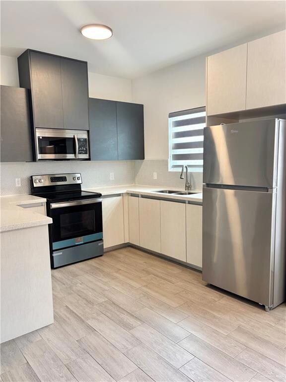Kitchen with stainless steel appliances, a sink, light countertops, backsplash, and light wood-style flooring