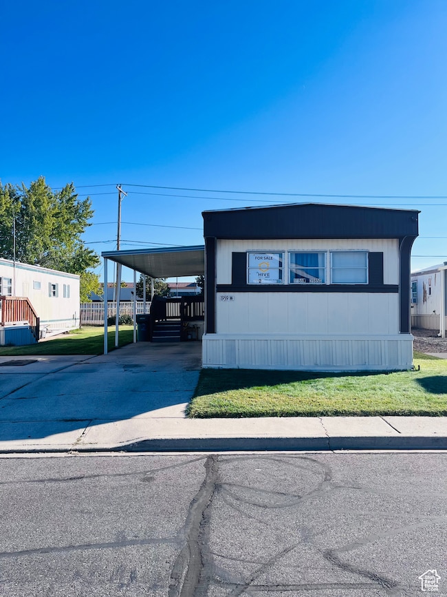 Manufactured / mobile home featuring driveway, an attached carport, a front lawn, and covered porch