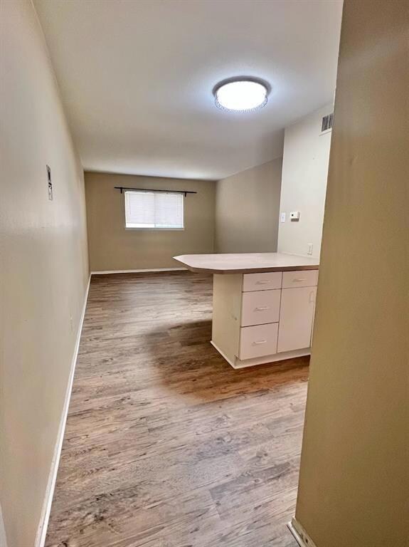 Kitchen featuring wood finished floors, white cabinetry, a peninsula, light countertops, and open floor plan