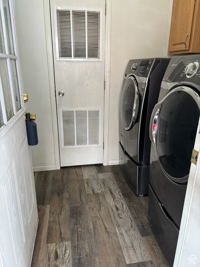 Laundry room with dark wood-style floors, washing machine and dryer, cabinet space, and a heating unit