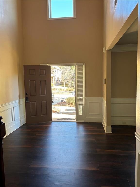 Foyer featuring healthy amount of natural light, a towering ceiling, wainscoting, dark wood-type flooring, and a decorative wall
