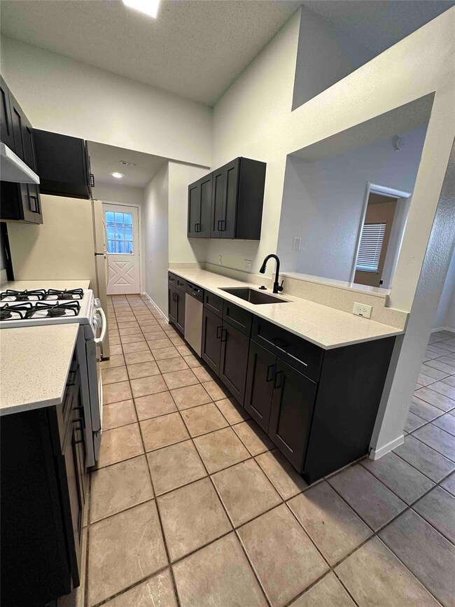 Kitchen with dark cabinetry, white range with gas cooktop, light stone countertops, and a textured ceiling