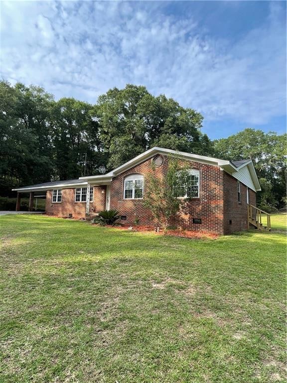 Ranch-style house featuring crawl space, brick siding, a front yard, an attached carport, and view of wooded area