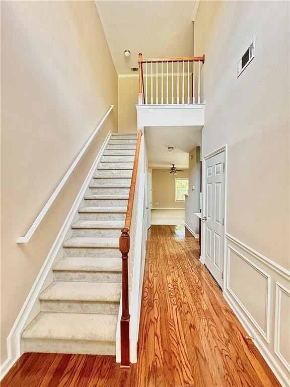 Stairway with wood finished floors, crown molding, a ceiling fan, and a high ceiling