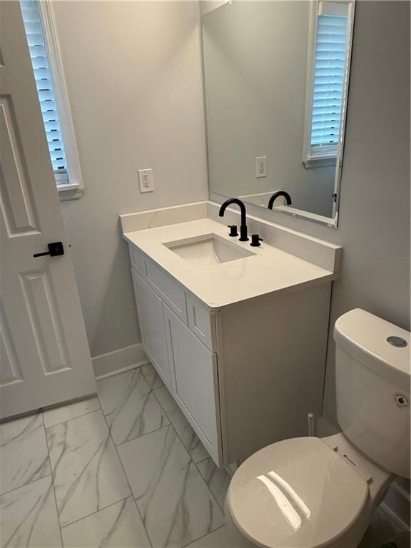 Half bath featuring vanity, light marble finish flooring, and healthy amount of natural light