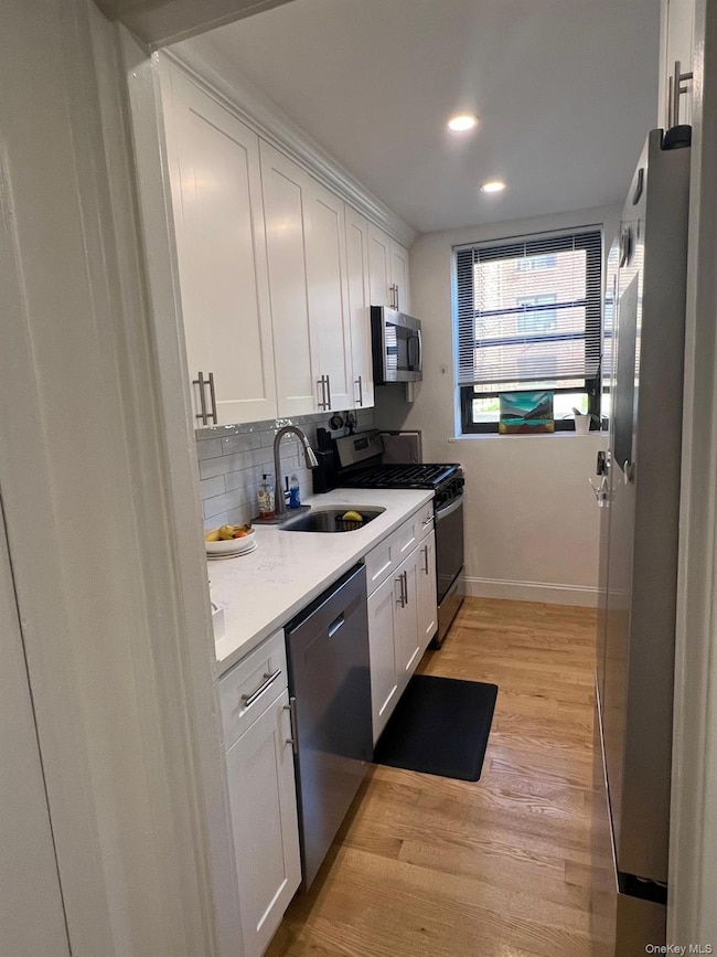 Kitchen with white cabinetry, appliances with stainless steel finishes, light wood flooring, backsplash, and recessed lighting