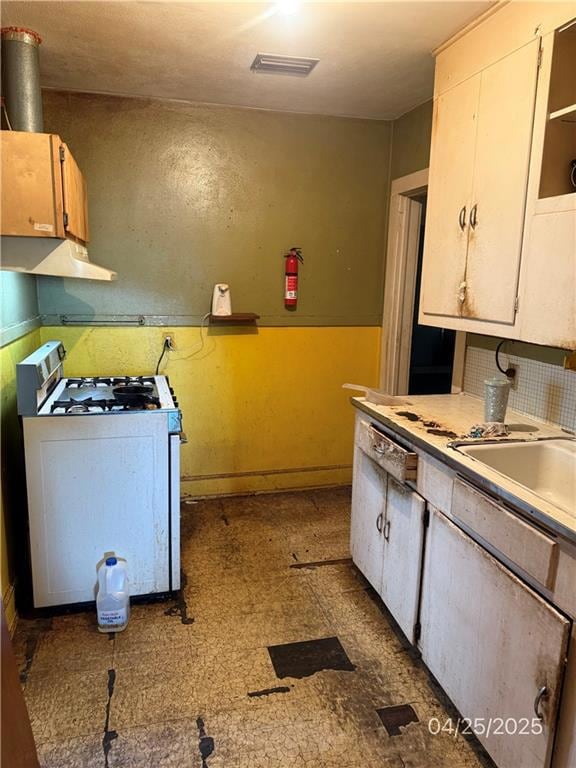 Kitchen with white gas range oven, under cabinet range hood, tile patterned floors, light countertops, and baseboards