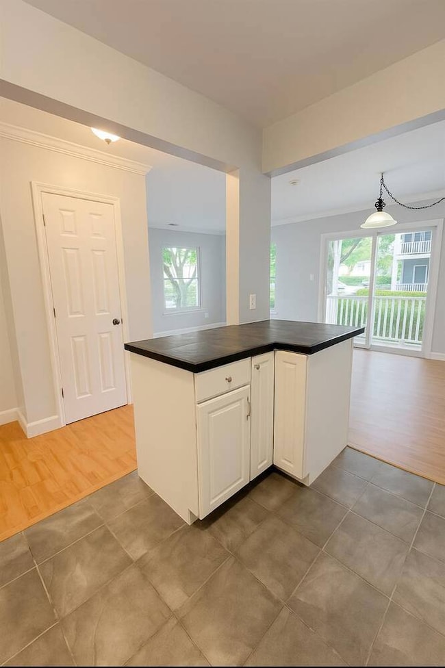 Kitchen featuring dark countertops, ornamental molding, healthy amount of natural light, white cabinets, and wood finished floors