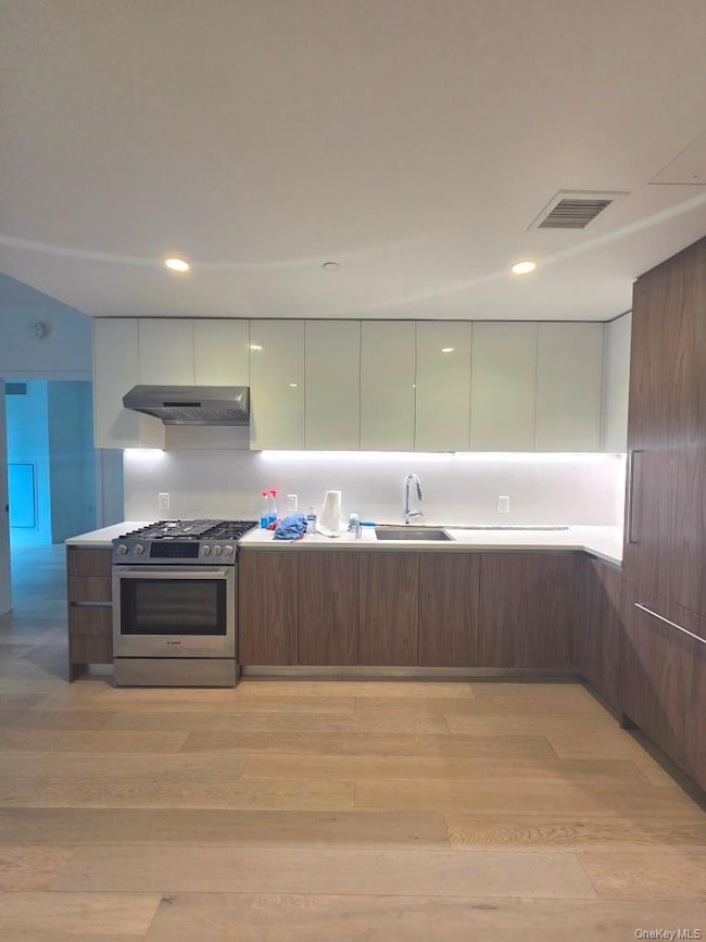 Kitchen with modern cabinets, stainless steel gas stove, light wood-style flooring, brown cabinetry, and recessed lighting