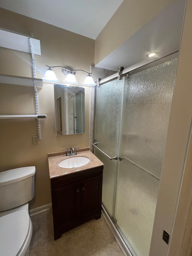 Full bathroom with toilet, a stall shower, vanity, and baseboards