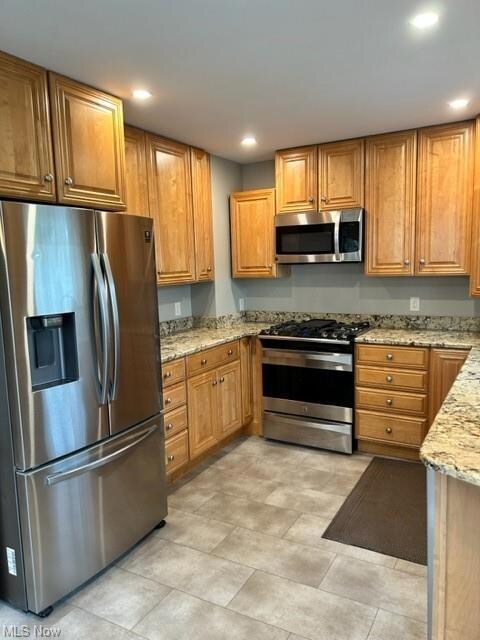 Kitchen with light tile flooring, light stone counters, refrigerator, and range