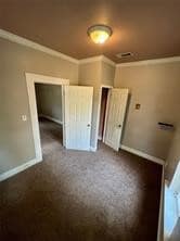 Unfurnished bedroom featuring crown molding and dark colored carpet