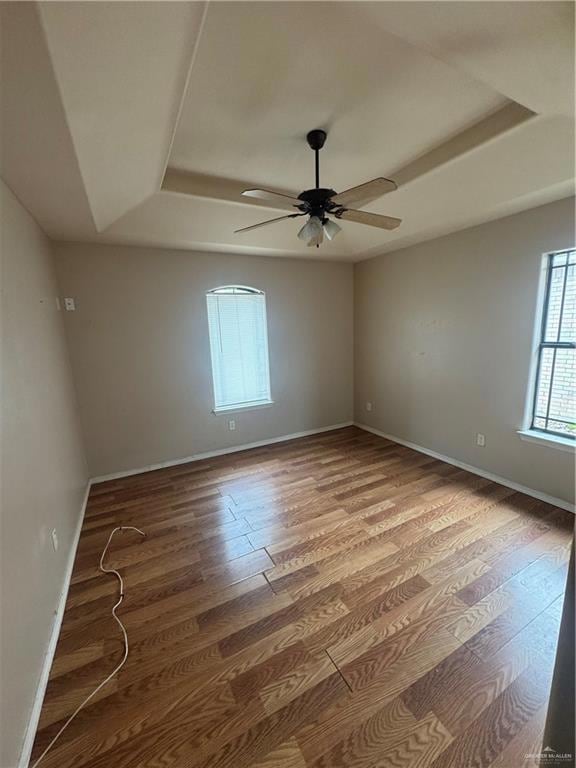 Spare room with a raised ceiling, wood finished floors, a ceiling fan, and baseboards