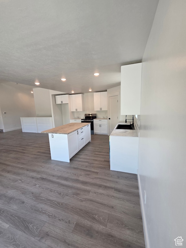Kitchen with butcher block counters, a sink, electric stove, white cabinetry, and dark wood finished floors