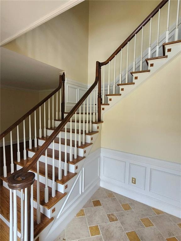 Staircase with a decorative wall, stone finish floors, a wainscoted wall, and crown molding