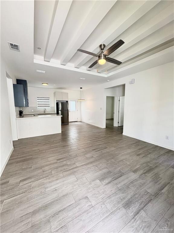 Unfurnished living room with ceiling fan, beam ceiling, wood finished floors, and baseboards
