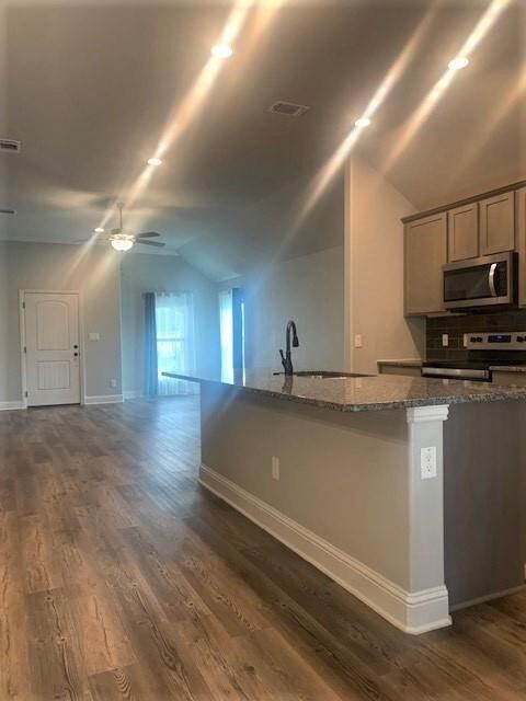 Kitchen featuring appliances with stainless steel finishes, a sink, vaulted ceiling, dark stone counters, and ceiling fan