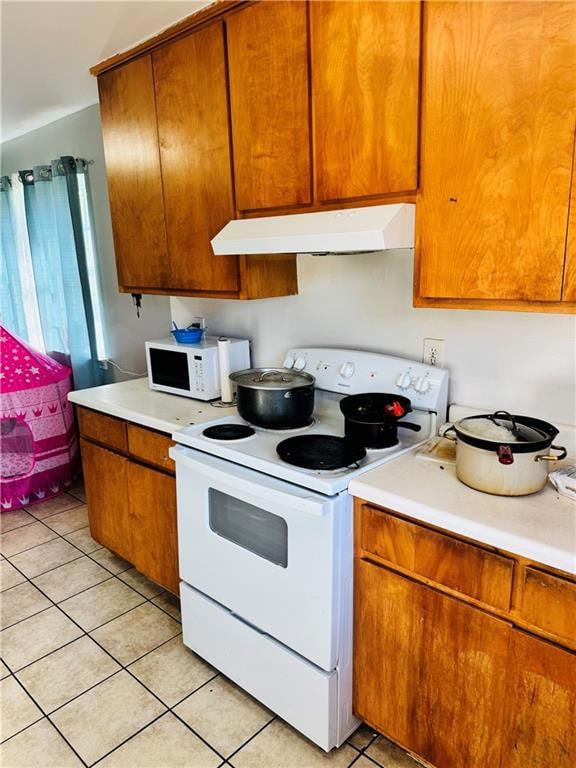 Kitchen with white appliances, brown cabinetry, light countertops, and under cabinet range hood