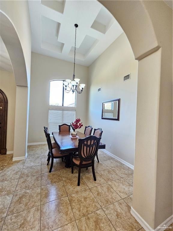 Dining area featuring arched walkways, coffered ceiling, a high ceiling, a chandelier, and beamed ceiling