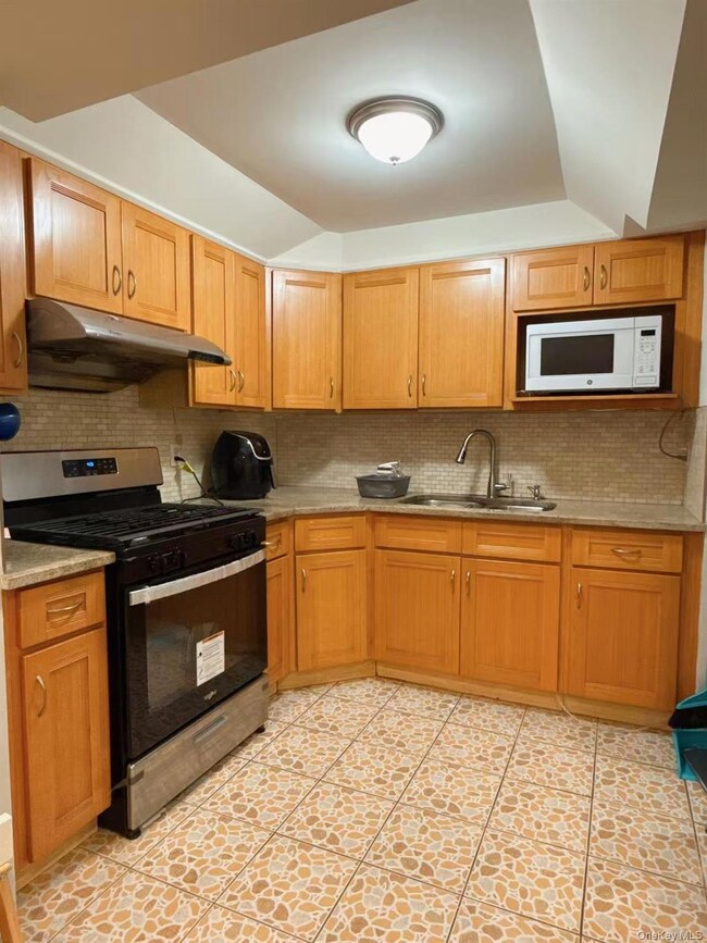 Kitchen with tasteful backsplash, stainless steel gas stove, white microwave, under cabinet range hood, and light tile patterned flooring
