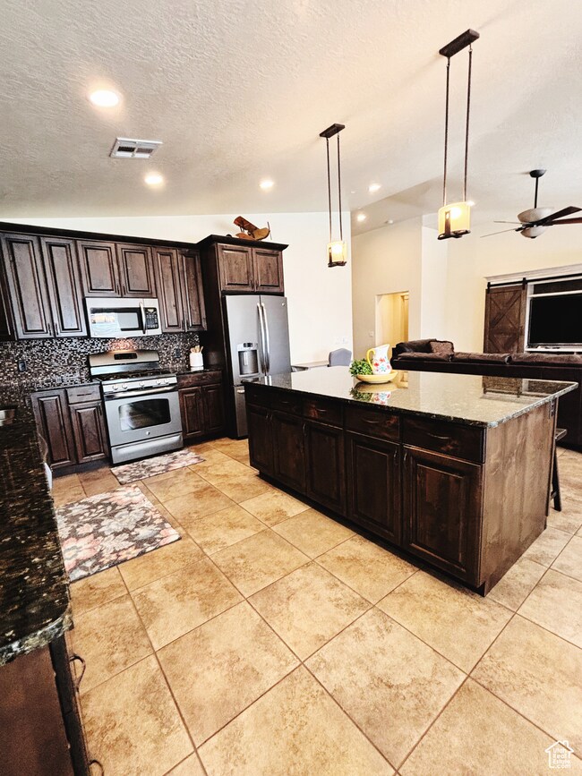 Kitchen with appliances with stainless steel finishes, a kitchen island, backsplash, pendant lighting, and open floor plan