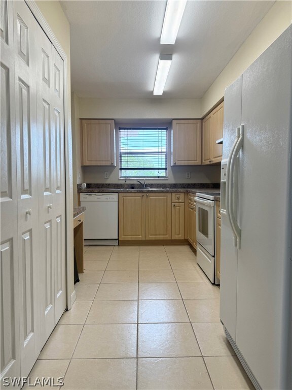 Kitchen with light tile patterned flooring, light brown cabinets, and white appliances