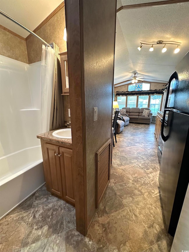 Full bathroom with vaulted ceiling, shower / bath combo, vanity, a textured ceiling, and ceiling fan