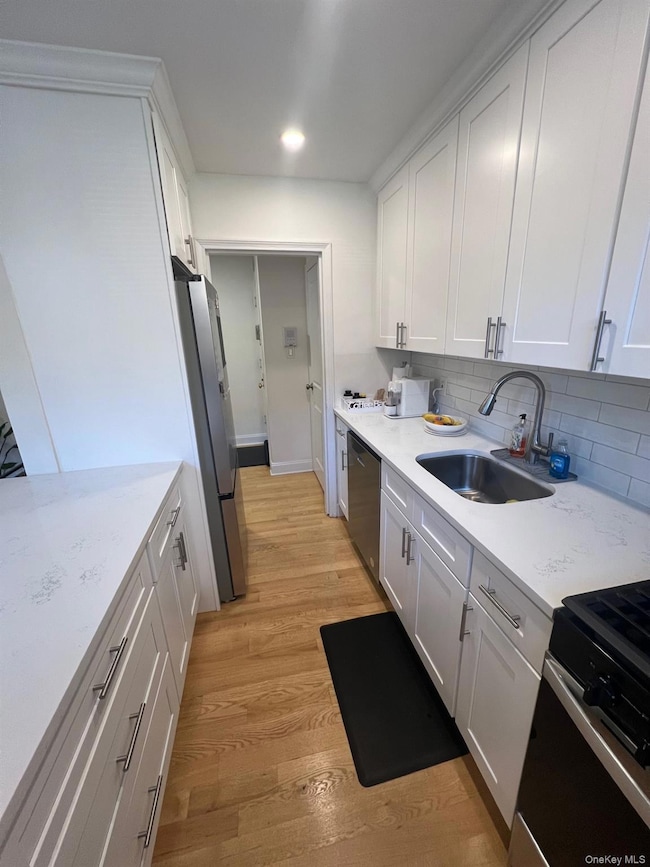 Kitchen with white cabinets, stainless steel appliances, light wood floors, backsplash, and light stone counters