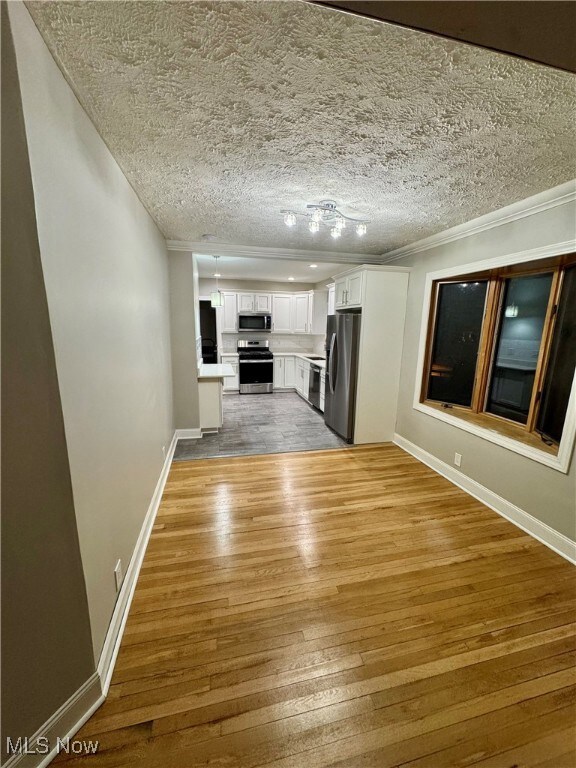 Unfurnished living room featuring a textured ceiling, crown molding, and light hardwood / wood-style floors