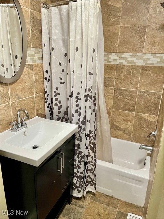 Full bath featuring vanity, shower / bath combination with curtain, tile walls, and stone tile flooring