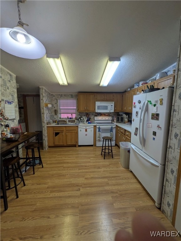 Kitchen with white appliances, light countertops, brown cabinets, light wood finished floors, and pendant lighting