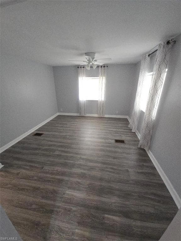 Unfurnished room with ceiling fan, dark wood-type flooring, and baseboards