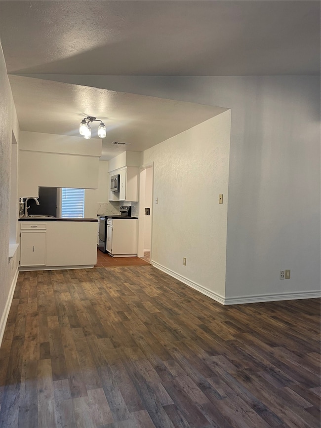 Unfurnished living room featuring dark wood-style flooring and baseboards