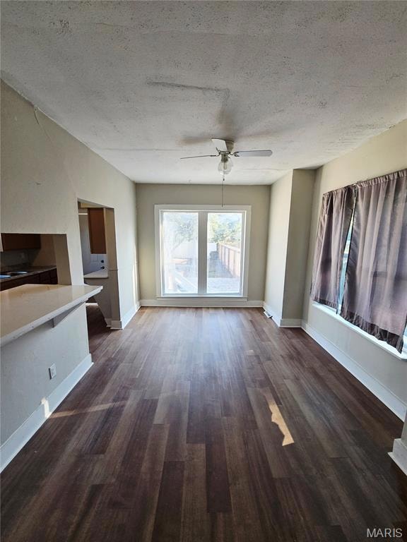 Unfurnished living room with a textured ceiling, dark wood-type flooring, and a ceiling fan