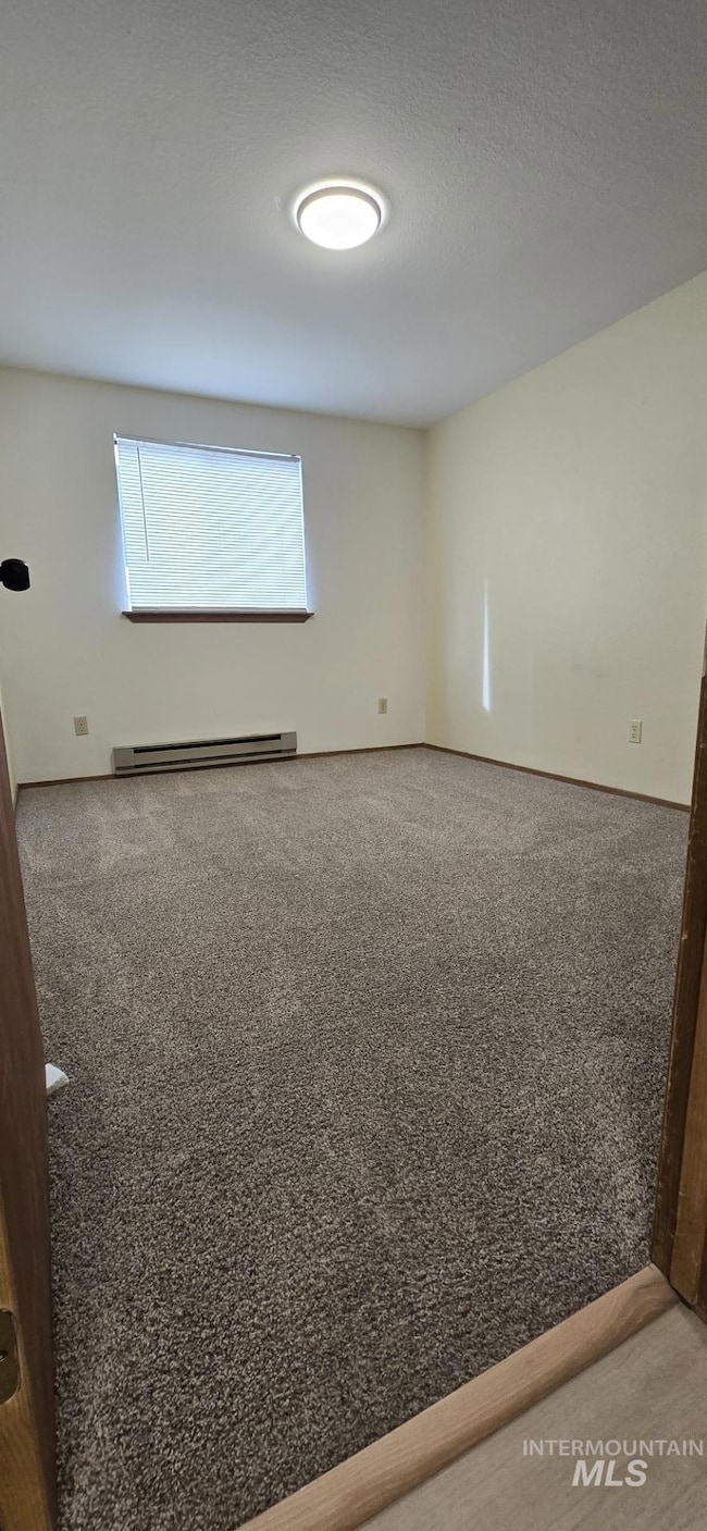 Spare room featuring a textured ceiling, a baseboard heating unit, and light colored carpet