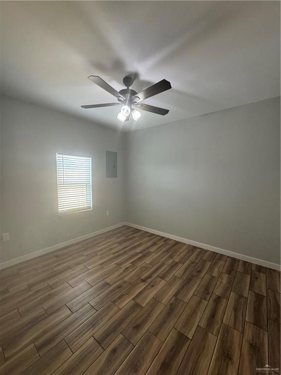 Unfurnished room with electric panel, dark wood-style floors, baseboards, and a ceiling fan