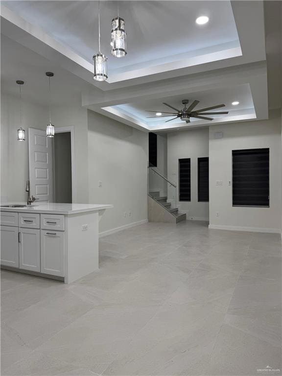 Unfurnished living room featuring a raised ceiling, recessed lighting, ceiling fan, and stairway