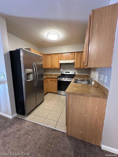 Kitchen featuring appliances with stainless steel finishes, light tile patterned floors, brown cabinets, light colored carpet, and light countertops