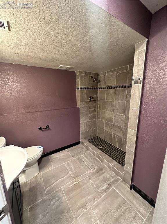 Full bathroom with a textured wall, vanity, a tile shower, and a textured ceiling