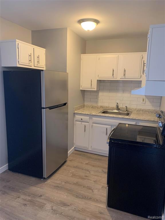 Kitchen featuring freestanding refrigerator, black electric range, backsplash, light wood finished floors, and white cabinets